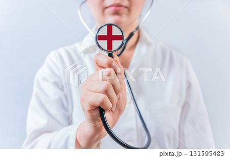 Female doctor holding stethoscope with England flag. National health system of England Female doctor holding stethoscope with England flag. National health system of England 131595483