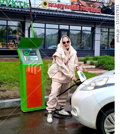 Smiling woman charging a white electric car at green station. 131597931