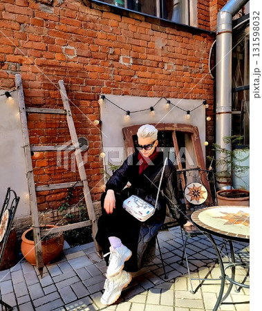 Stylish woman relaxing outdoors at vintage brick wall cafe. 131598032