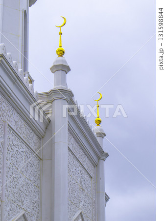 The walls of the mosque with golden crescents and carved white marble walls against the backdrop of a cloudy dawn sky The walls of the mosque with golden crescents and carved white marble walls against the backdrop of a cloudy dawn sky 131598844