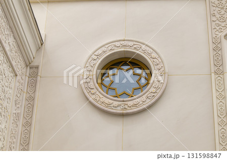 A round window with floral ornamentation and a carved frame on the white marble wall of the mosque A round window with floral ornamentation and a carved frame on the white marble wall of the mosque 131598847