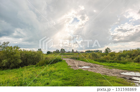 Muddy rural road with puddles and a fork under an overcast sky, countryside landscape 131598869