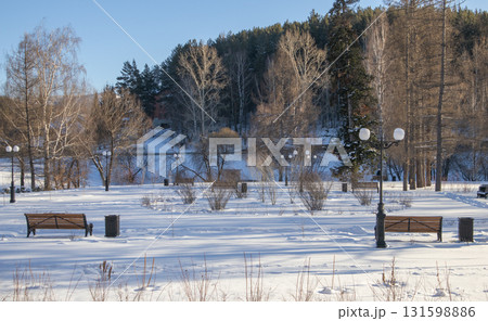 Winter park with benches and lampposts in snow, long shadows and blue sky Winter park with benches and lampposts in snow, long shadows and blue sky 131598886
