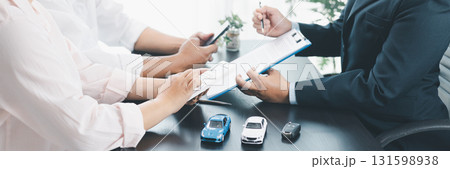 Panorama view of business meeting with car loan agreement, dealer showing calculator to customers at office desk with vehicle model and key, concept of auto finance, leasing or insurance. car loan. Panorama view of business meeting with car loan agreement, dealer showing calculator to customers at office desk with vehicle model and key, concept of auto finance, leasing or insurance. car loan. 131598938