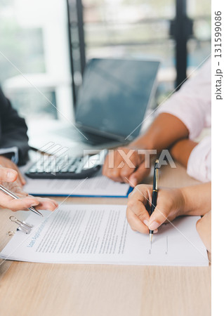 Close up of business people signing loan agreement contract with pen and paperwork on desk, financial deal concept with laptop and calculator in modern office environment. loan agreement contract. Close up of business people signing loan agreement contract with pen and paperwork on desk, financial deal concept with laptop and calculator in modern office environment. loan agreement contract. 131599086