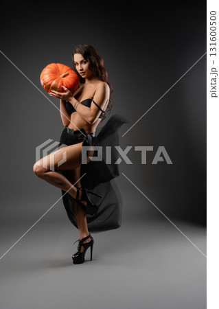 Woman poses confidently in black attire holding pumpkin with artistic lighting Woman poses confidently in black attire holding pumpkin with artistic lighting 131600500