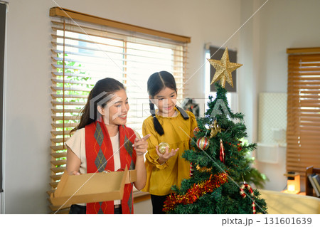 Mother and child decorating a Christmas tree together to celebrate the upcoming holiday season. Family celebration in winter holiday / New Year season Mother and child decorating a Christmas tree together to celebrate the upcoming holiday season. Family celebration in winter holiday / New Year season 131601639