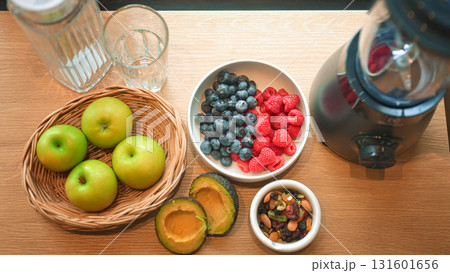 Healthy lifestyle setup in the kitchen. Fresh fruits apples, blueberries, raspberries, and avocado arranged beside a blender, prepared for making a homemade smoothie Healthy lifestyle setup in the kitchen. Fresh fruits apples, blueberries, raspberries, and avocado arranged beside a blender, prepared for making a homemade smoothie 131601656