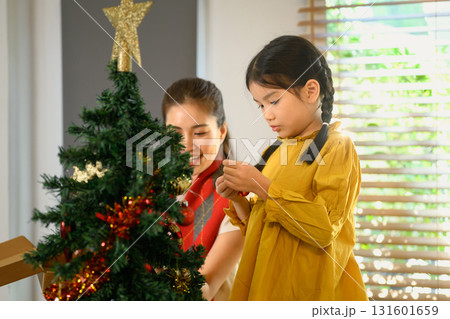 Mother and child decorating a Christmas tree together to celebrate the upcoming holiday season. Family celebration in winter holiday / New Year season 131601659