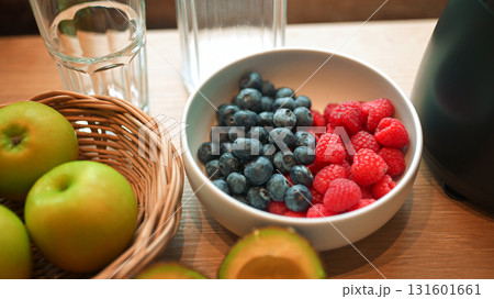 Healthy lifestyle setup in the kitchen. Fresh fruits apples, blueberries, raspberries, and avocado arranged beside a blender, prepared for making a homemade smoothie 131601661