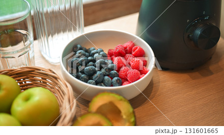 Healthy lifestyle setup in the kitchen. Fresh fruits apples, blueberries, raspberries, and avocado arranged beside a blender, prepared for making a homemade smoothie 131601665