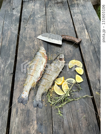Fresh trout on a rustic wooden board with a knife. Natural light highlights the texture of the fish and wood. Fresh trout on a rustic wooden board with a knife. Natural light highlights the texture of the fish and wood. 131603106