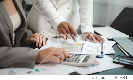 Two businesswomen analyzing financial reports and charts using calculator in modern office 131605442