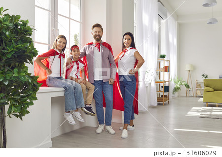 Happy family in superhero costumes standing near the windowsill at home and looking at camera. Happy family in superhero costumes standing near the windowsill at home and looking at camera. 131606029