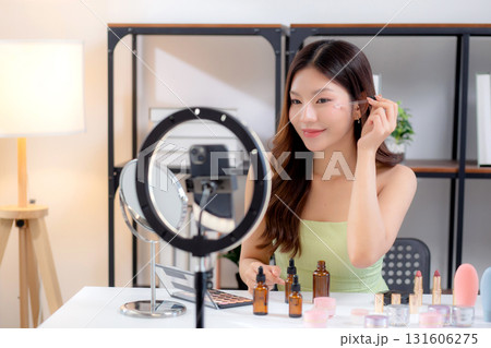 Young asian woman demonstrating serum on face on social media at home. 131606275