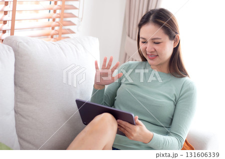 Young asian woman sitting on sofa using digital tablet computer for video call in living room. 131606339
