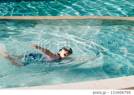 Child Playing Joyfully in Swimming Pool Water Wearing Goggles and Swimming Trunks in Bright Sunlight Splashing Water with Excitement Child Playing Joyfully in Swimming Pool Water Wearing Goggles and Swimming Trunks in Bright Sunlight Splashing Water with Excitement 131606798