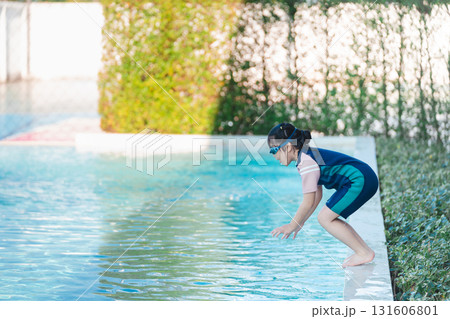 Young child preparing to dive into a refreshing pool water, wearing swim gear and goggles, sunny day with greenery in the background, summer fun at home Young child preparing to dive into a refreshing pool water, wearing swim gear and goggles, sunny day with greenery in the background, summer fun at home 131606801