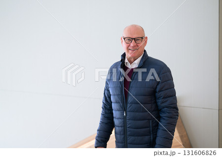 Portrait of a happy senior man smiling at the camera while standing indoors wearing blue jacket Portrait of a happy senior man smiling at the camera while standing indoors wearing blue jacket 131606826