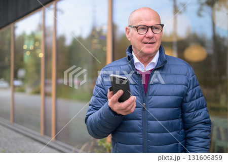 Elderly man in a blue jacket and glasses is using a mobile phone 131606859
