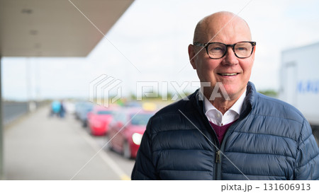 Happy senior Scandinavian man standing outdoors in front of a car park at an airport taxi area 131606913