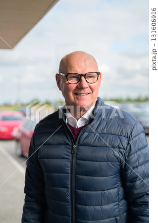 Happy senior Scandinavian man standing outdoors in front of a car park at an airport taxi area 131606916
