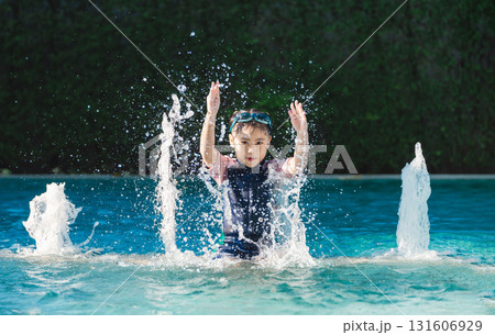 Happy child playing in swimming pool, splashing water with hands raised, enjoying summer day under bright sunlight with playful energy and joy Happy child playing in swimming pool, splashing water with hands raised, enjoying summer day under bright sunlight with playful energy and joy 131606929
