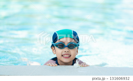 Happy child with swim goggles smiling in water while holding onto pool edge, enjoying a playful summer day in bright sunlight and clear water 131606932