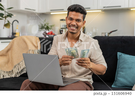 Indian man checks dollar cash with laptop spreadsheet enters sums confirm goal smiles bonus invest Indian man checks dollar cash with laptop spreadsheet enters sums confirm goal smiles bonus invest 131606940