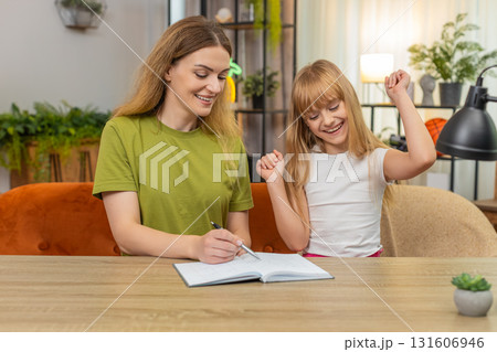 Mother daughter play tic tac toe on paper rounds keep score notebook laugh rematch at table together Mother daughter play tic tac toe on paper rounds keep score notebook laugh rematch at table together 131606946