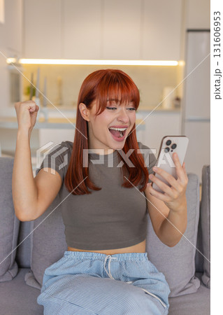 Young woman with smartphone gets good news jumps with joy celebrates win smiles and cheers indoors 131606953