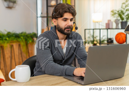Indian man with headset and mic at laptop polite support agent listens and writes notes in notebook Indian man with headset and mic at laptop polite support agent listens and writes notes in notebook 131606960