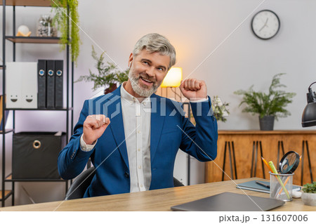 Middle-aged businessman dances on chair wearing earphones singing rock music after working on laptop Middle-aged businessman dances on chair wearing earphones singing rock music after working on laptop 131607006