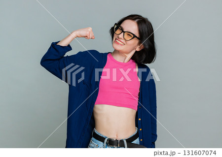 Young woman confidently raising arms showing biceps with proud smile symbolizing strength and power 131607074