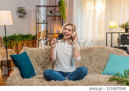 Adult woman singing with headphones and microphone at home dancing joyfully feeling like a superstar 131607098