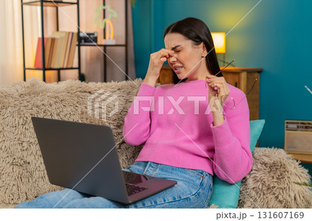 Young woman closing laptop after long work removing glasses rubbing eyes tired from screen fatigue Young woman closing laptop after long work removing glasses rubbing eyes tired from screen fatigue 131607169
