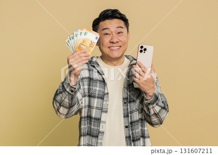 Happy Asian man use smartphone rejoicing game win, receiving money euro cash, celebrating success 131607211