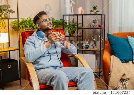 Attractive smiling Indian man drinking a cup of coffee or herbal tea at home chair in the morning Attractive smiling Indian man drinking a cup of coffee or herbal tea at home chair in the morning 131607224