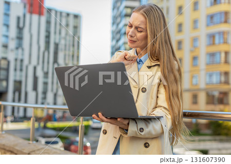 Mature Caucasian woman on laptop in downtown street sees bad lottery results, looking disappointed 131607390