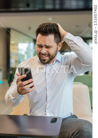 Young businessman using mobile phone becomes shocked sudden lottery results in office hotel lobby 131607402