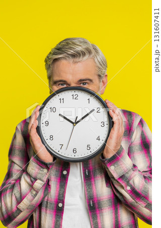 Mature man hiding behind large office clock, playful peek, cautious glance, time awareness humor Mature man hiding behind large office clock, playful peek, cautious glance, time awareness humor 131607411