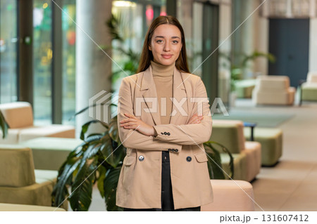 Portrait of happy young businesswoman with arms crossed looking at camera in office hotel lobby Portrait of happy young businesswoman with arms crossed looking at camera in office hotel lobby 131607412