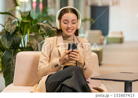 Excited young businesswoman in headphones listening energetic music on smartphone in office lobby 131607413
