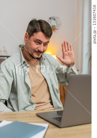 Smiling young man freelancer having video call via laptop sitting at home office desk in living room 131607416