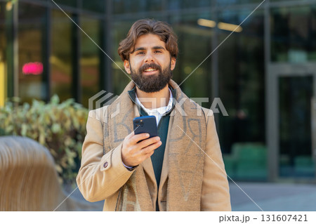 Happy young business man using smartphone and looking at camera while standing in downtown street 131607421