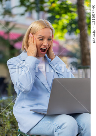 Happy mature businesswoman using laptop computer celebrating success victory clenching fists in city 131607440