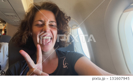 Happy passenger young woman is flying in plane. Smiling girl sitting in airplane near window going on trip vacation travel. Traveling female inside plane enjoying flight. Traveling girl 131607945
