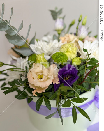 Elegant floral arrangement in a pastel box with purple ribbon, featuring white chrysanthemums, purple lisianthus, peach eustoma, and greenery. Perfect for gift, celebration, or wedding decor. Elegant floral arrangement in a pastel box with purple ribbon, featuring white chrysanthemums, purple lisianthus, peach eustoma, and greenery. Perfect for gift, celebration, or wedding decor. 131608103