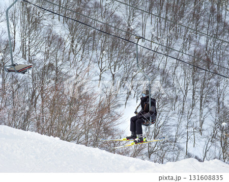 スキー場でシングルリフトに乗り雪山の林間を進む一人のスキーヤー (新潟県、斑尾高原) 131608835