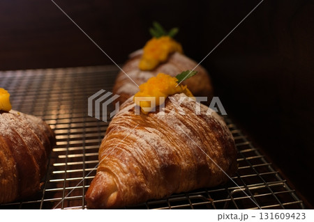A tray of croissants filled with whipped cream and topped with sliced mango, displayed at a modern cafe bakery. A tray of croissants filled with whipped cream and topped with sliced mango, displayed at a modern cafe bakery. 131609423